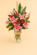 Bouquet of pink lilies and red roses in a clear vase on a beige background